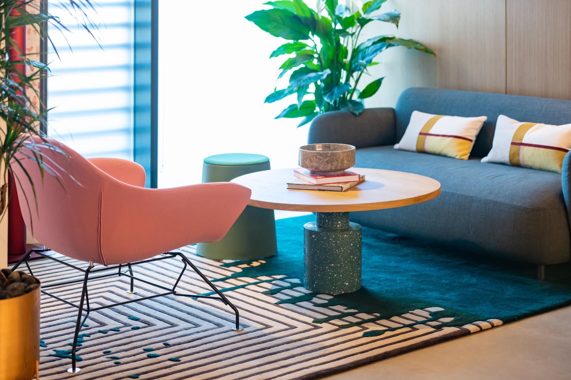 Stylish living space featuring a modern pink chair, wooden coffee table, vibrant rug, and lush indoor plants.