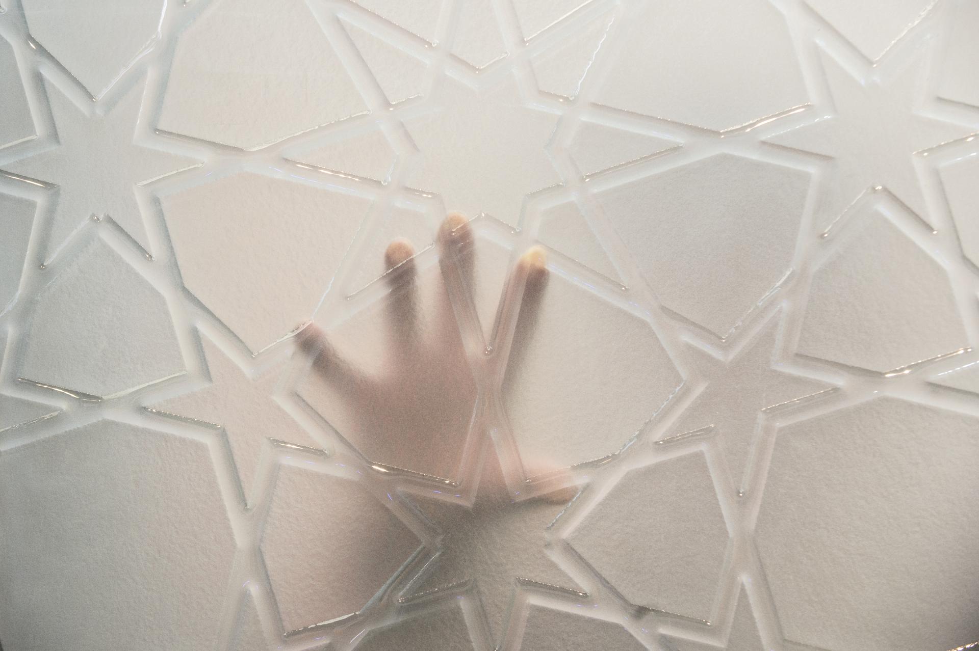 Intricate geometric surface design with a hand pressed against it, highlighting innovation in material textures.