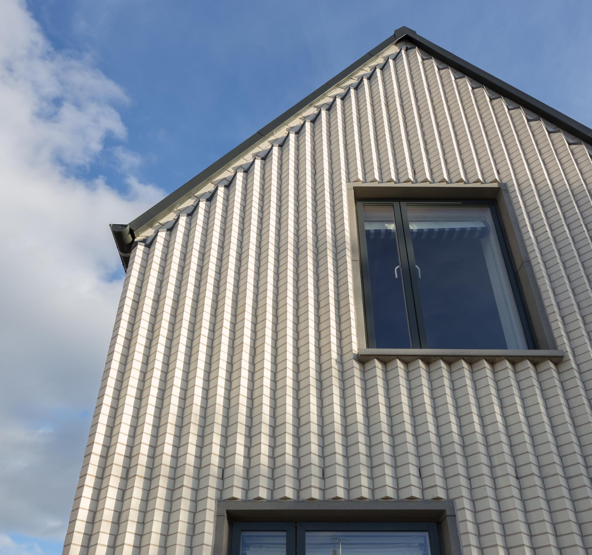 Contemporary architectural design of a textured, light-colored building featuring large windows against a blue sky.