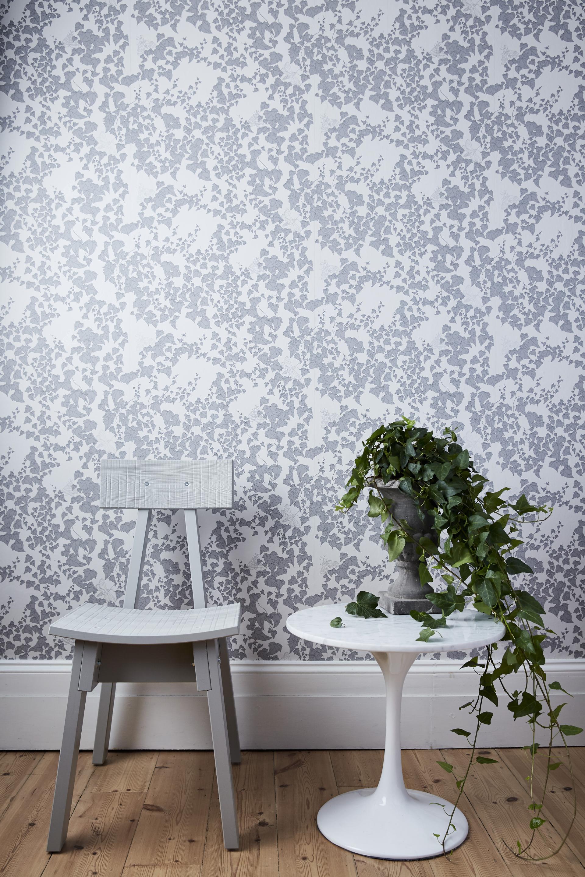 Elegant wallpaper design featuring foliage pattern, complemented by a grey chair and round marble-topped table with potted plant.