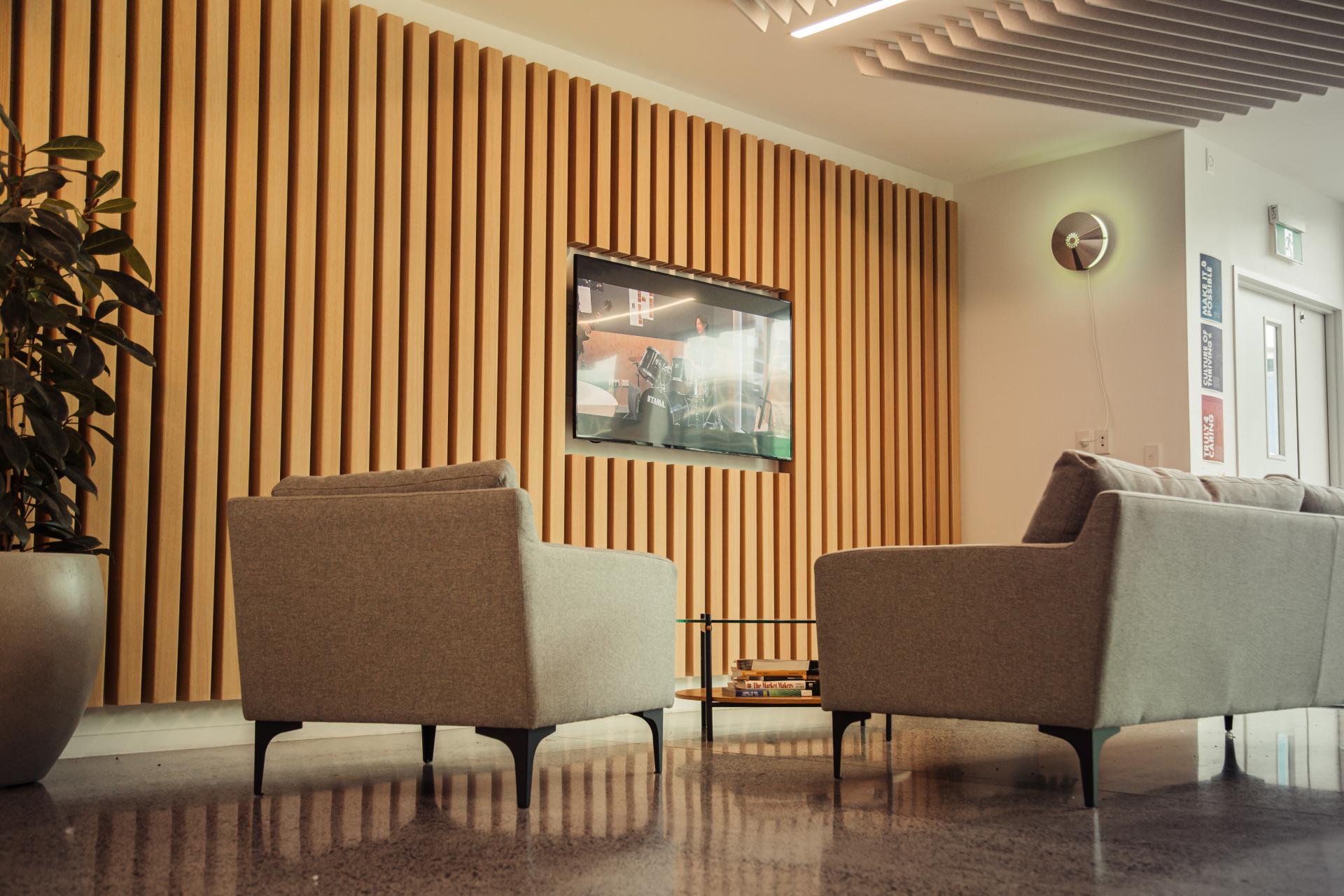 Modern lounge with acoustic timber wall, gray armchairs, and a television, creating a stylish sound-absorbing interior.