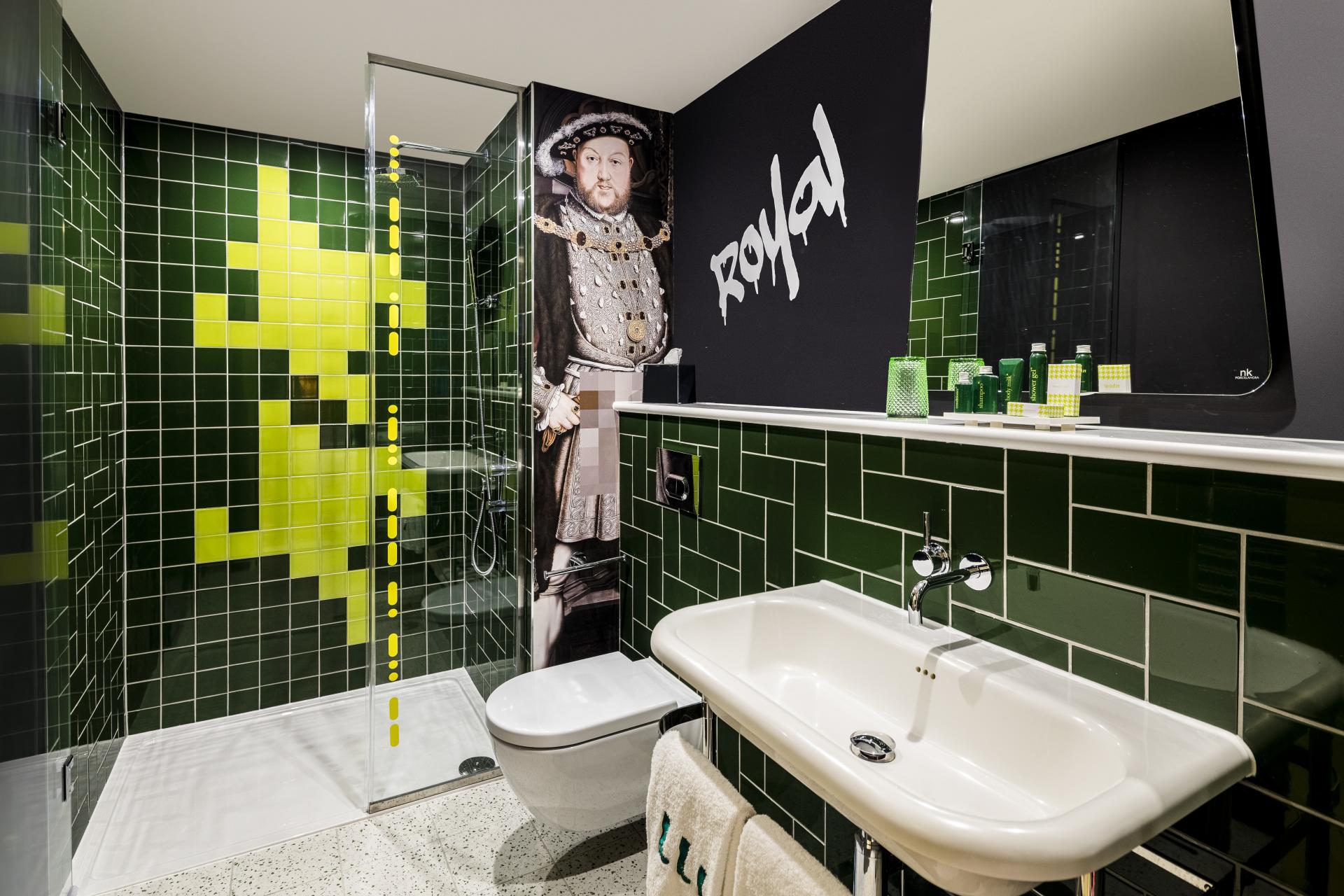 Stylish hotel bathroom featuring green tiles, modern fixtures, and a mural of Henry VIII at nhow London.