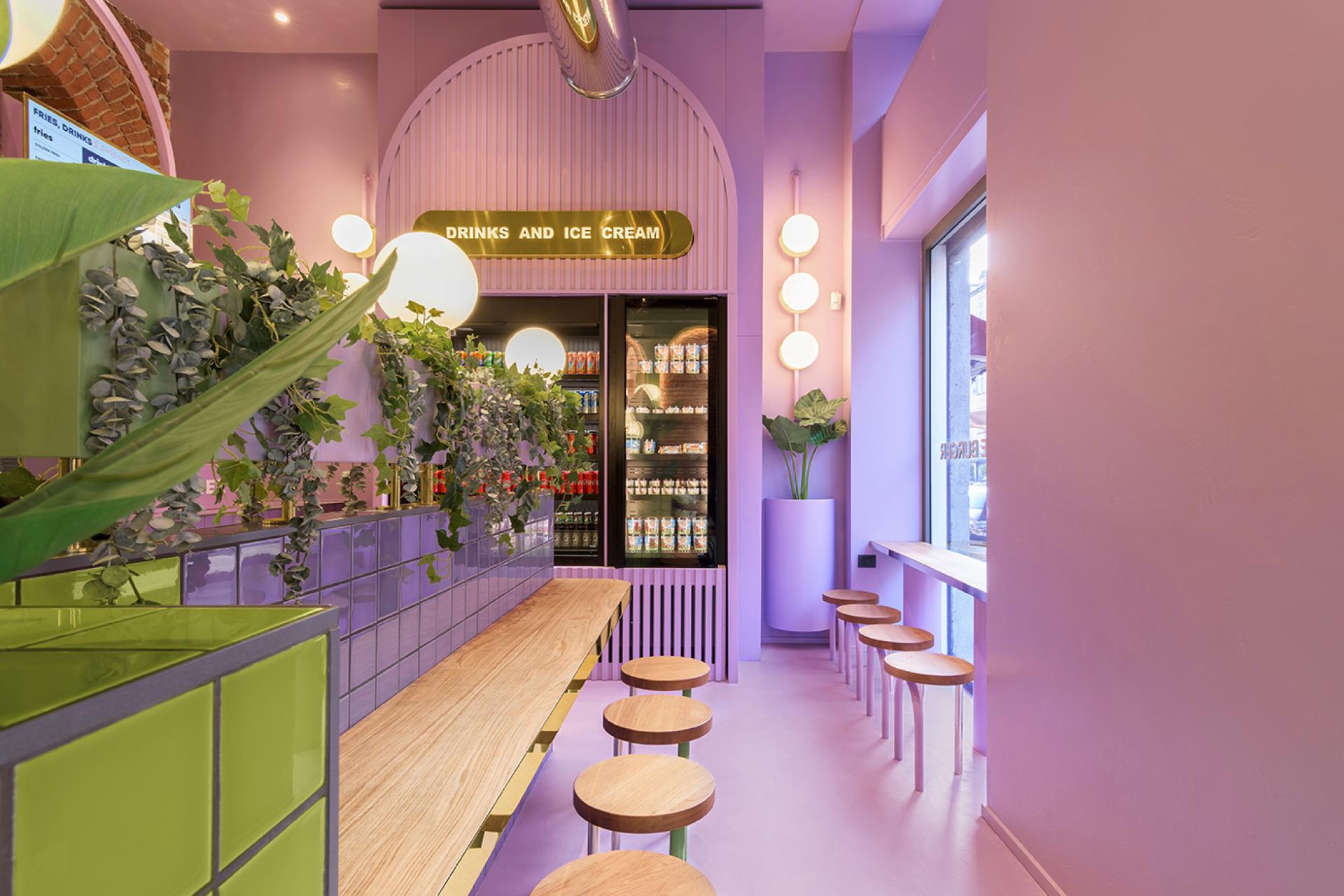 Bright candy-coloured interior of Bun in Milan featuring a wooden bench, plants, and a drink display.