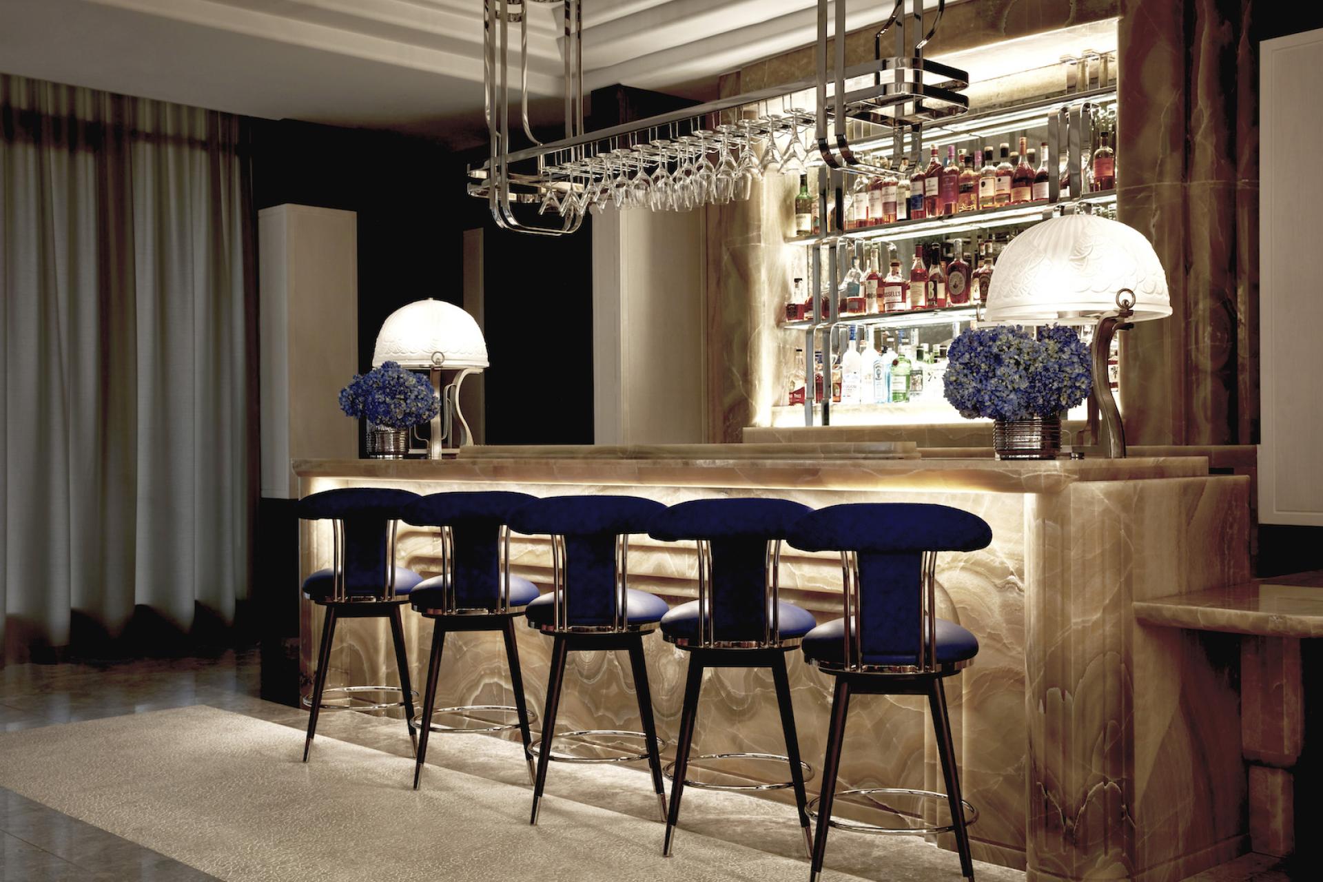 Elegant bar area featuring blue velvet seats, Art Deco elements, and a stunning display of spirits at The Maybourne Bar.