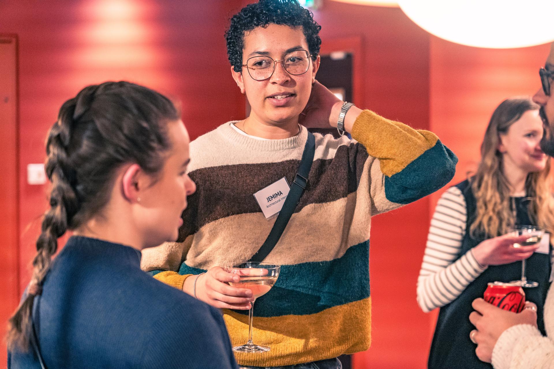 A diverse group of professionals networking at a seminar on net zero carbon buildings, with drinks in hand.