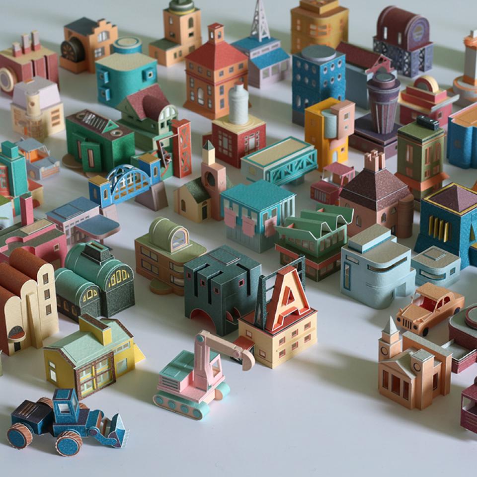 Colorful miniature buildings and vehicles crafted by Charles Young, showcasing intricate model making in his paper metropolis project.
