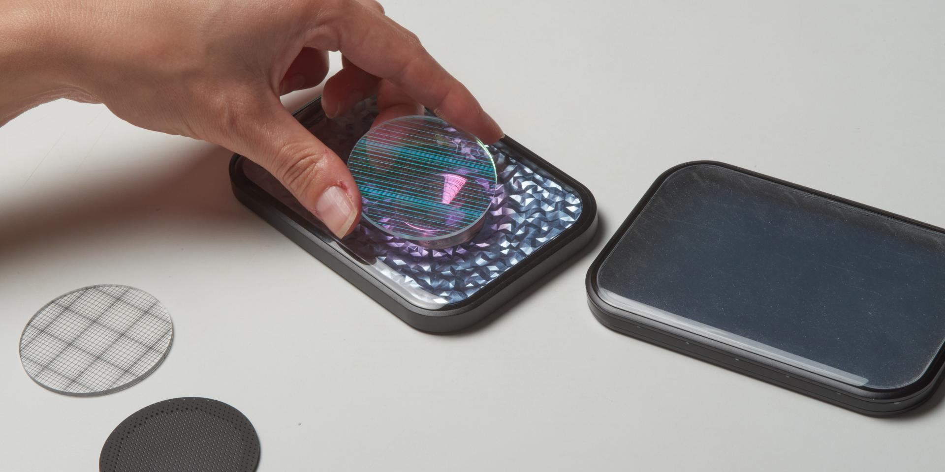 A hand pressing a colorful, textured lens onto a reflective surface, illustrating innovative CMF design and material exploration.