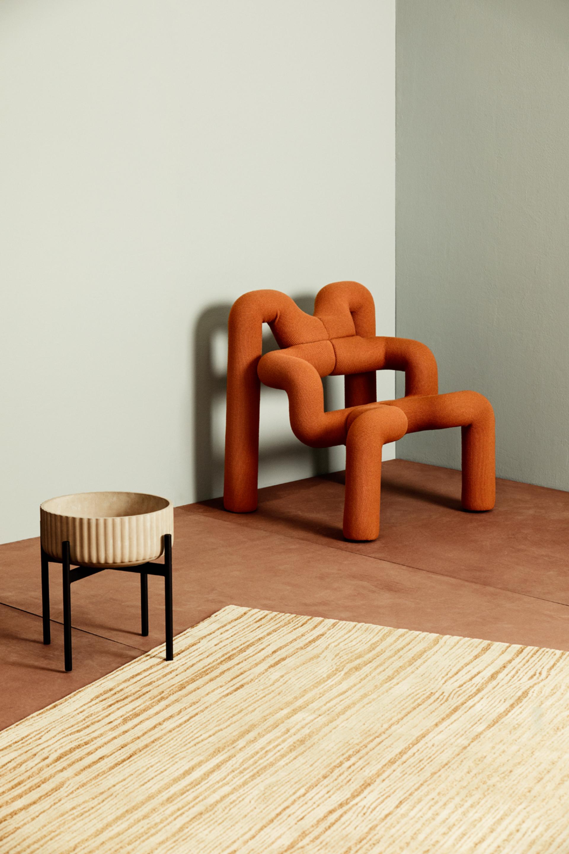 Sustainable Norwegian design featuring an orange sculptural chair and a wooden planter in a minimalist setting.
