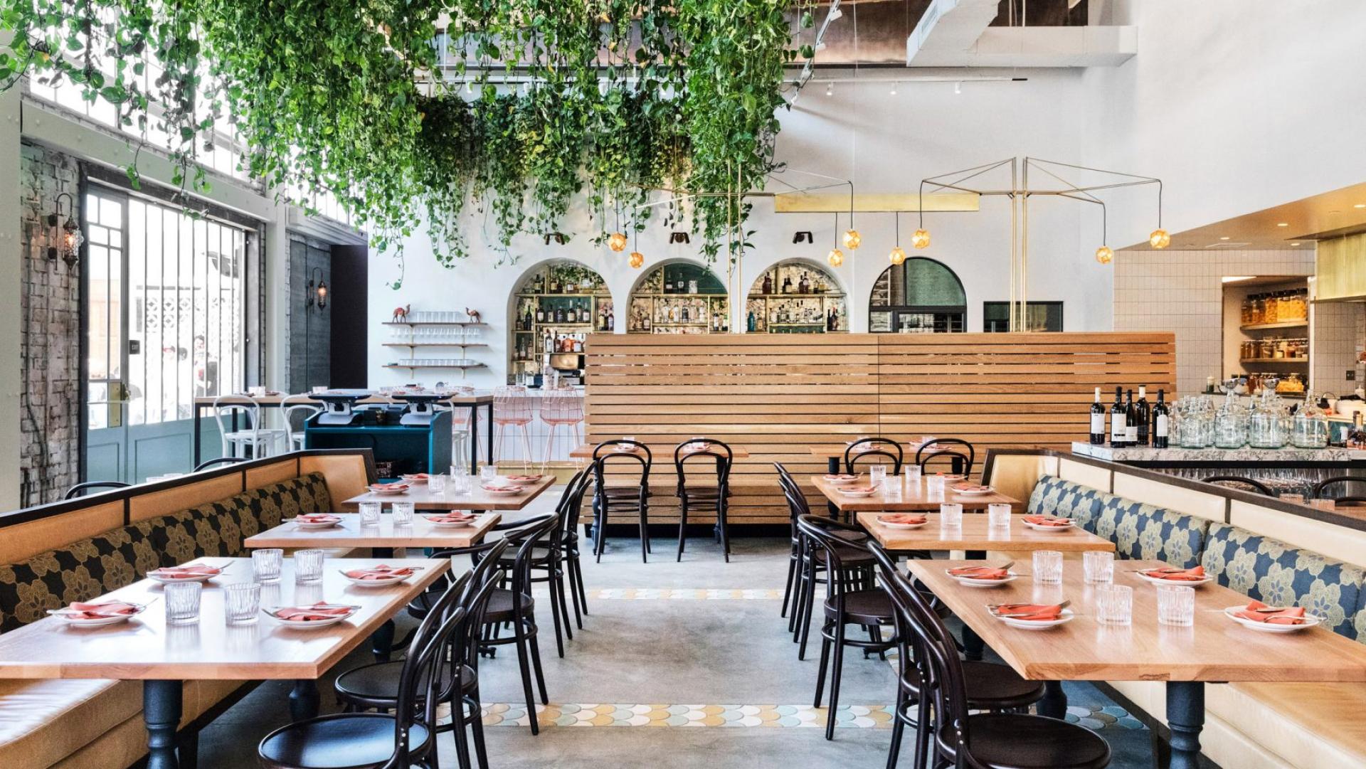 Stylish interior of Bavel restaurant featuring wooden furniture, vibrant decor, and lush greenery, designed by Studio Unltd.