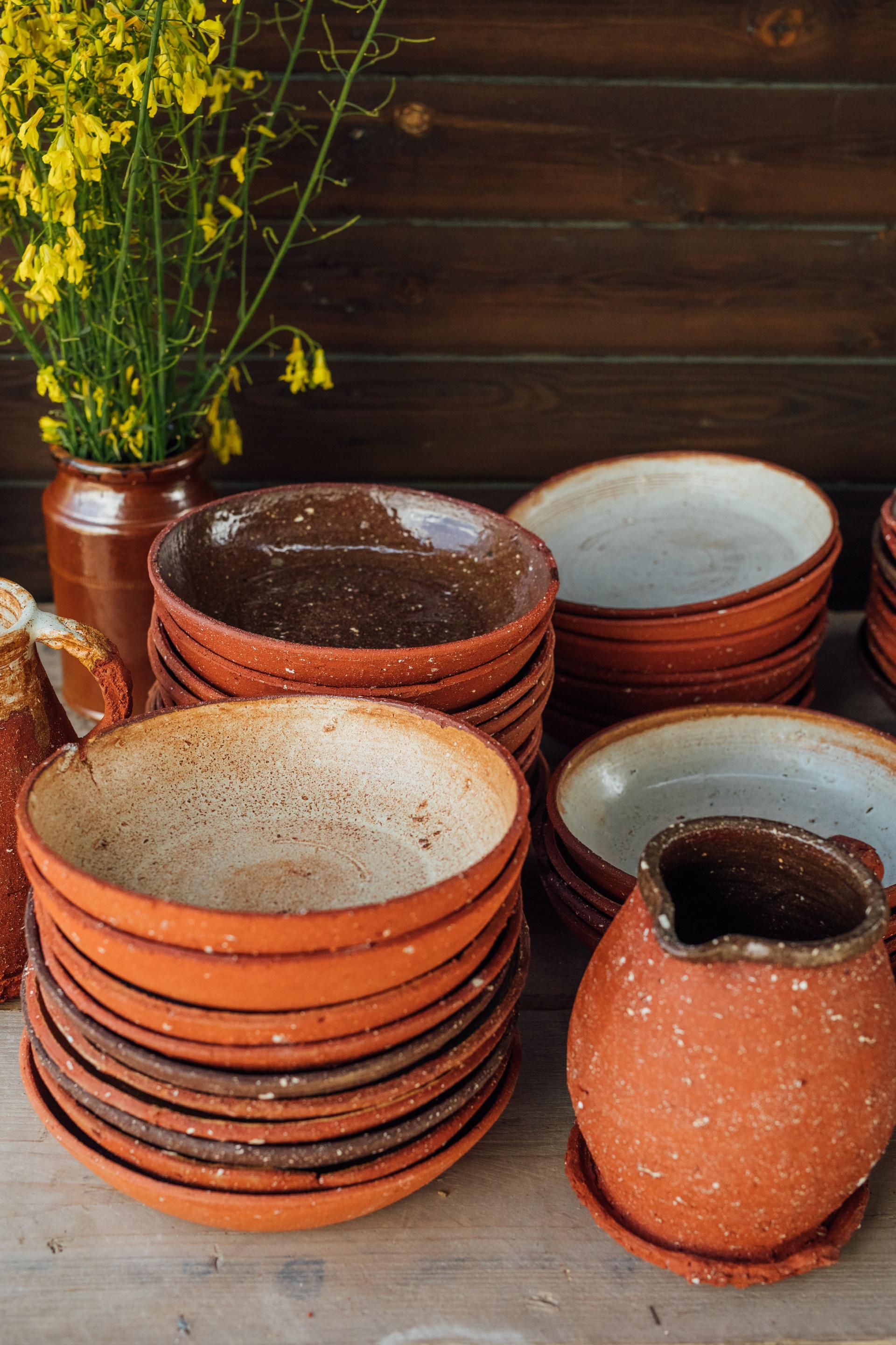 Handcrafted pottery pieces in earthy tones stacked beside floral arrangements, highlighting Bruno Schooling's artistic craftsmanship.