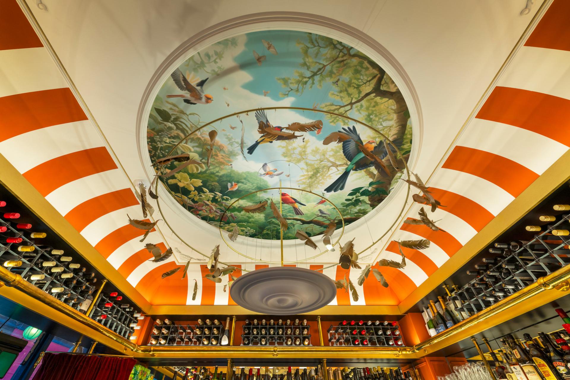 Vibrant ceiling design with suspended bird motifs and colorful stripes in a compact Brixton bar.