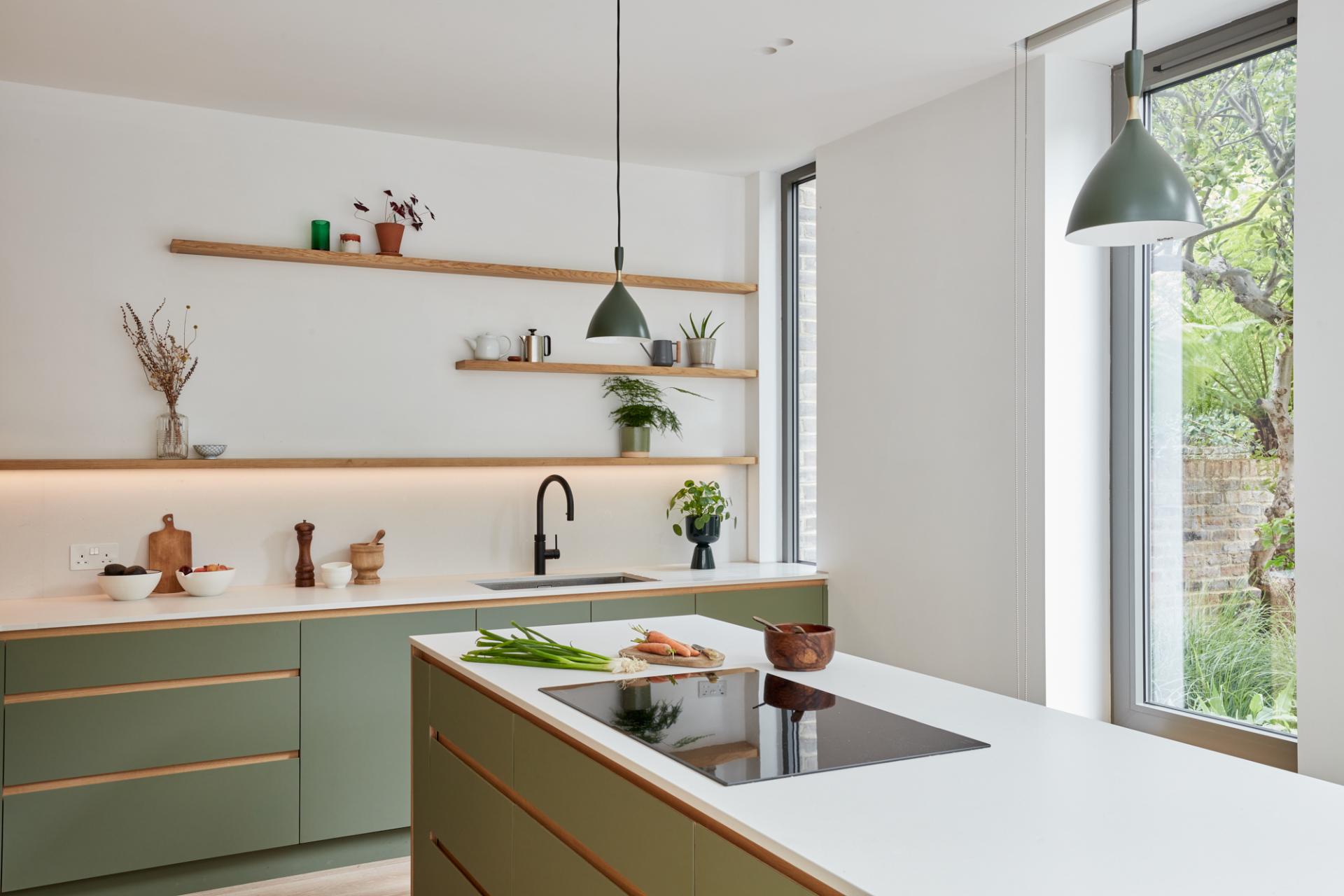 Modern kitchen featuring natural wood elements, green cabinetry, and bright windows overlooking lush greenery outside.
