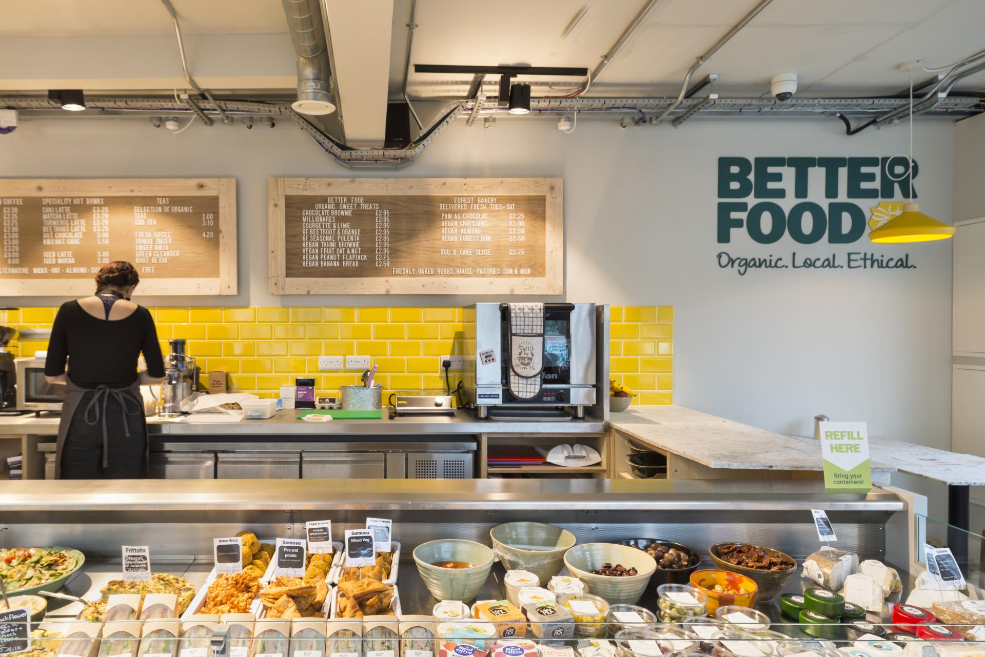 Modern café-deli at Better Food featuring organic menu items, bright yellow tiles, and a well-stocked display counter.