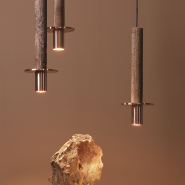 Three pendant lights made from stone and copper illuminate a natural rock on a minimalist pedestal.