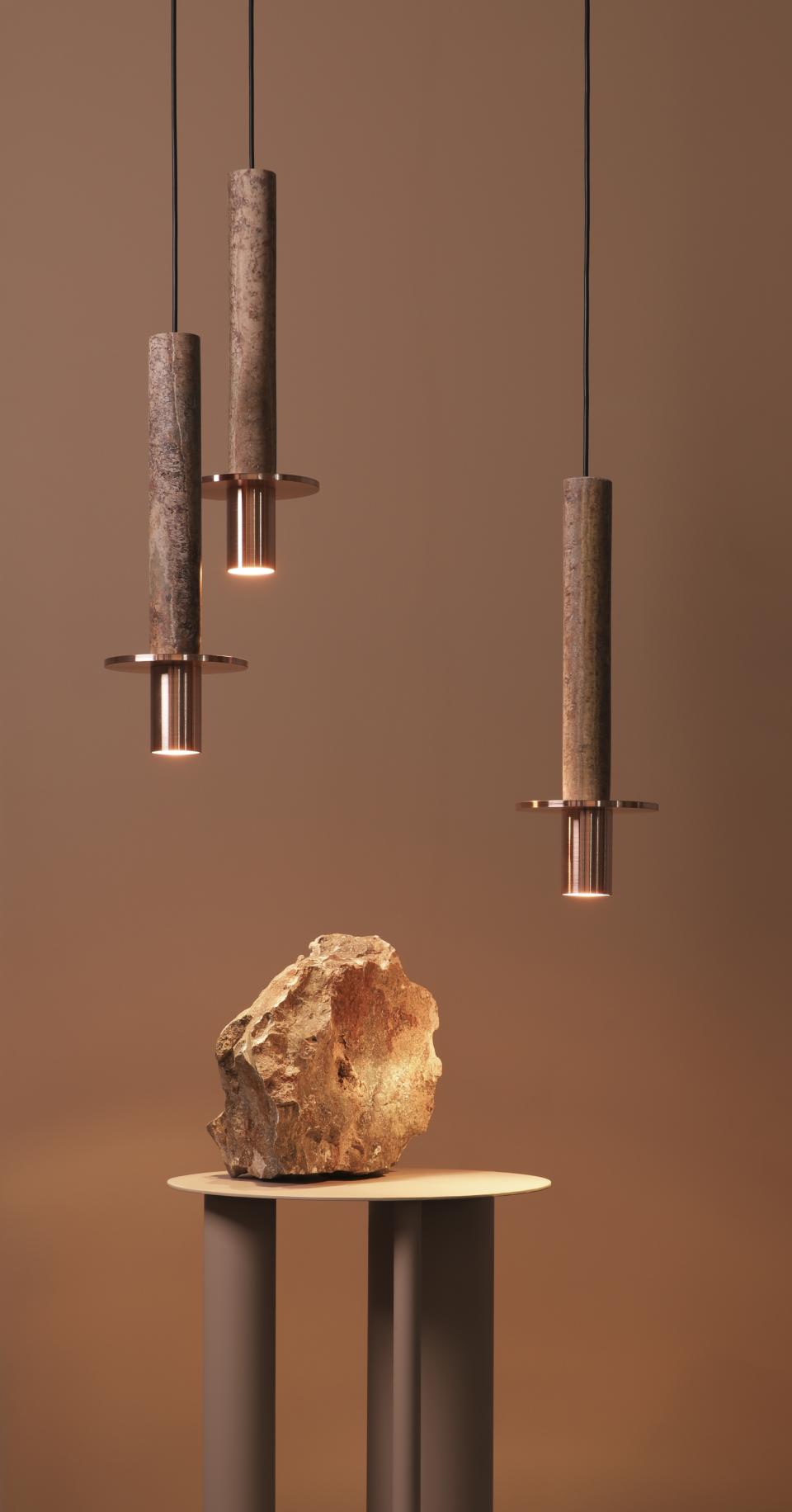 Three pendant lights made from stone and copper illuminate a natural rock on a minimalist pedestal.