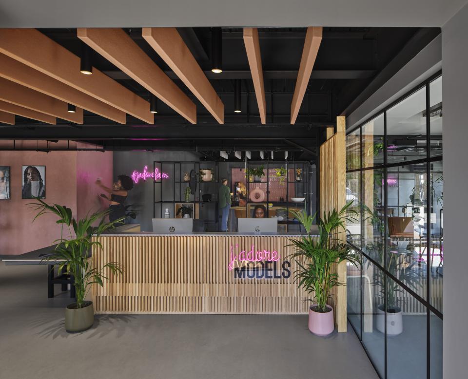 Modern reception area of J’adore Models featuring stylish design elements, neon signage, and greenery by Workshop Design Studio.