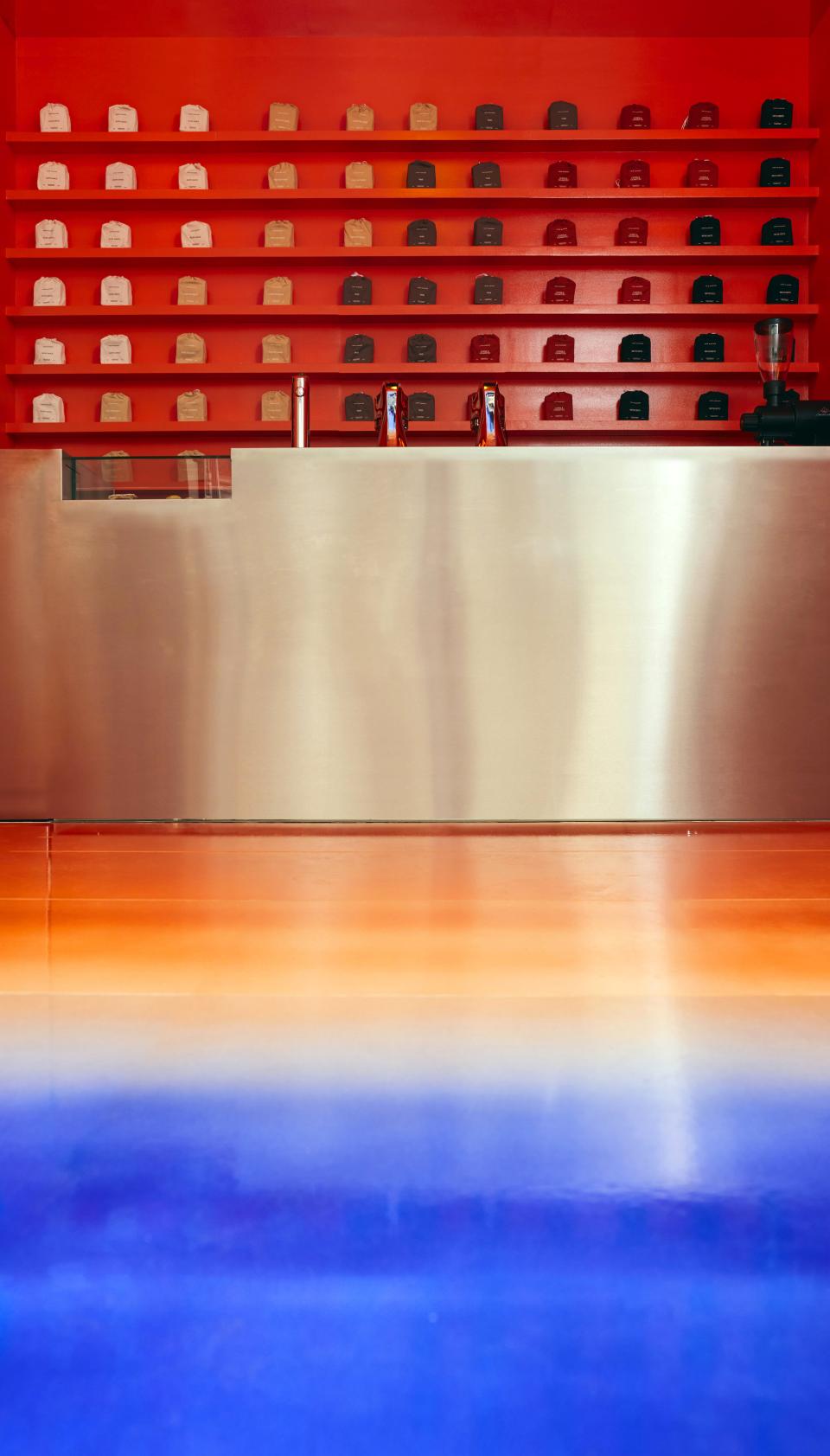Vibrant café interior with orange and blue flooring, featuring an artistic shelving display of various tea packages.