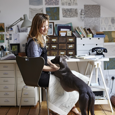 Abigail Edwards interacts with her dog in her inspiring, nature-themed design studio filled with wallpaper samples.