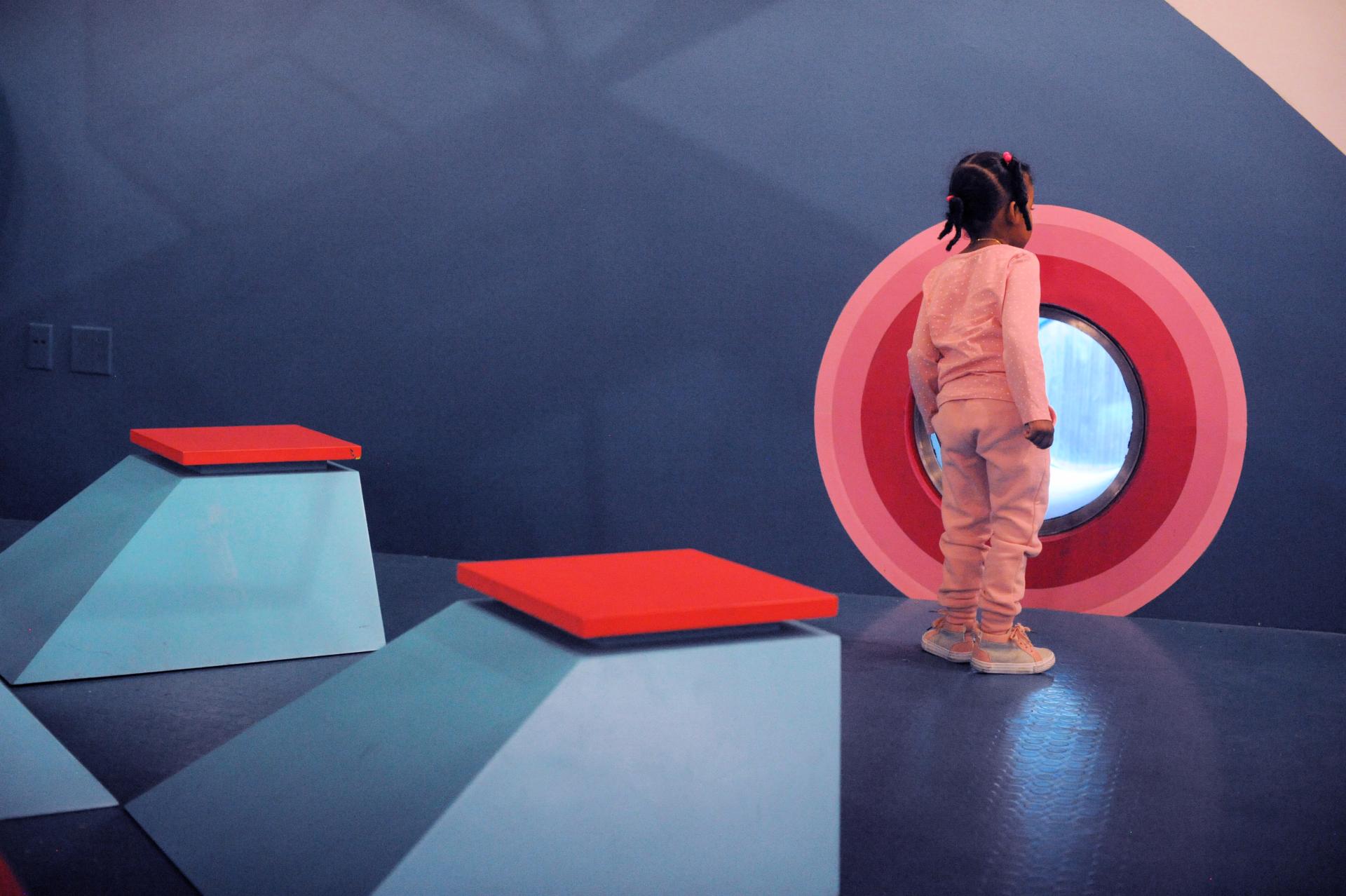 Brightly colored art space featuring a young girl looking through a circular window at ColorLab in Brooklyn.