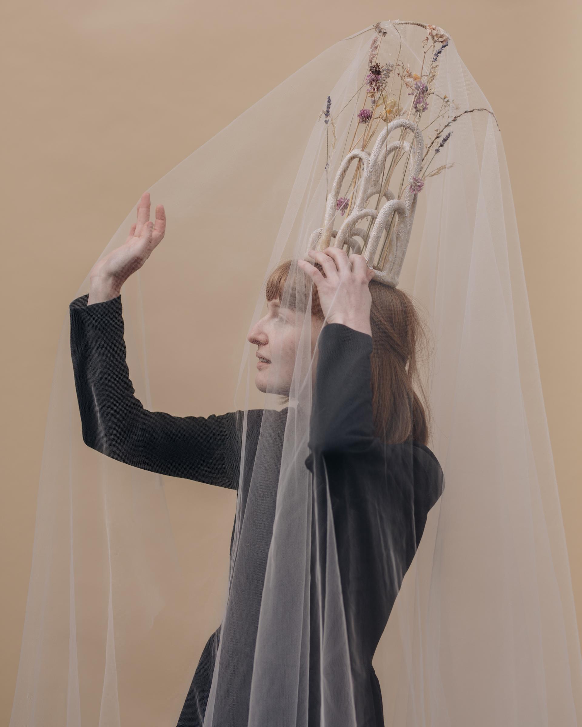 A model showcases an artistic headdress adorned with dried flowers and sheer fabric, emphasizing Glasgow's creative craft scene.