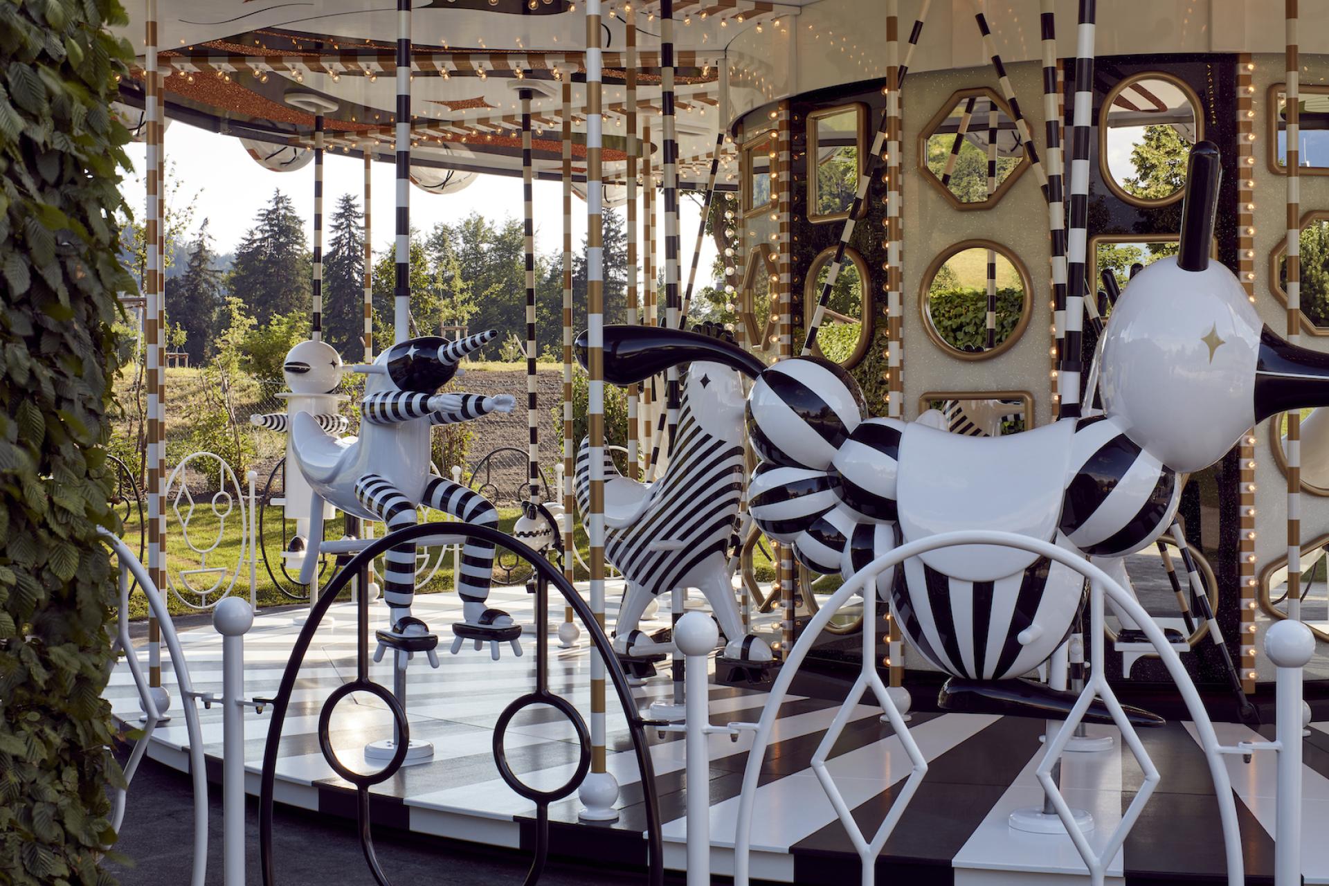 Colorful carousel featuring whimsical animal rides designed by Jaime Hayon, surrounded by lush greenery and bright lights.