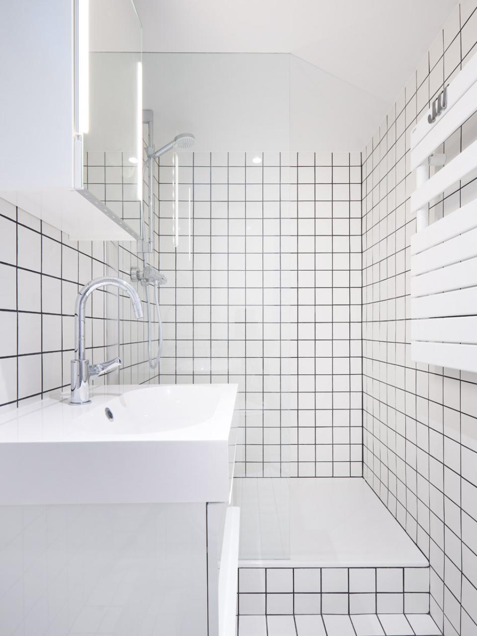Modern bathroom with black and white tiled walls, featuring a sleek sink and glass shower, designed for flexible living.