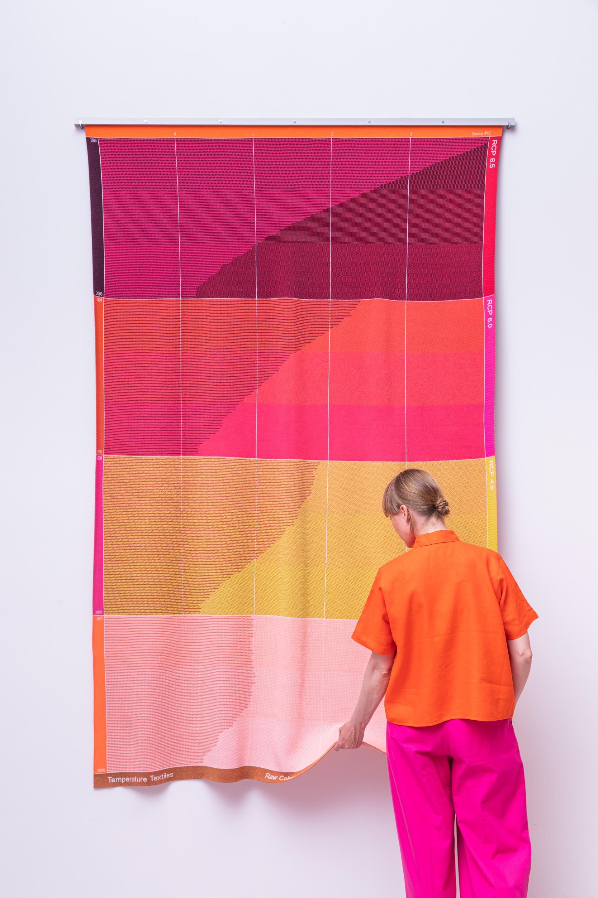 A woman interacts with a vibrant textile artwork showcasing bio-based color palettes by Raw Color.