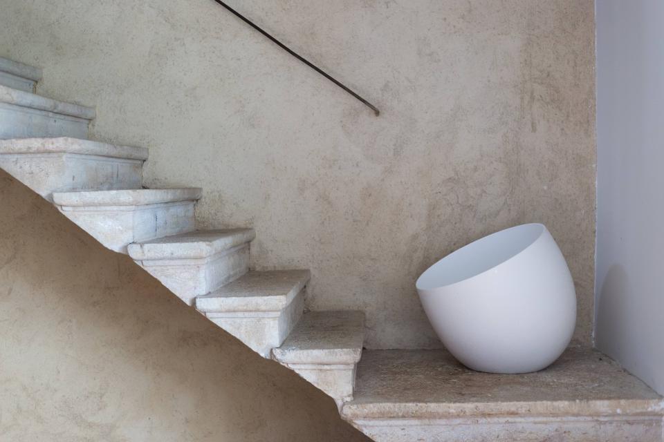 Modern white ceramic light fixture rests against a textured wall beside elegant stone stairs, showcasing innovative design by Faïencerie de Charolles.