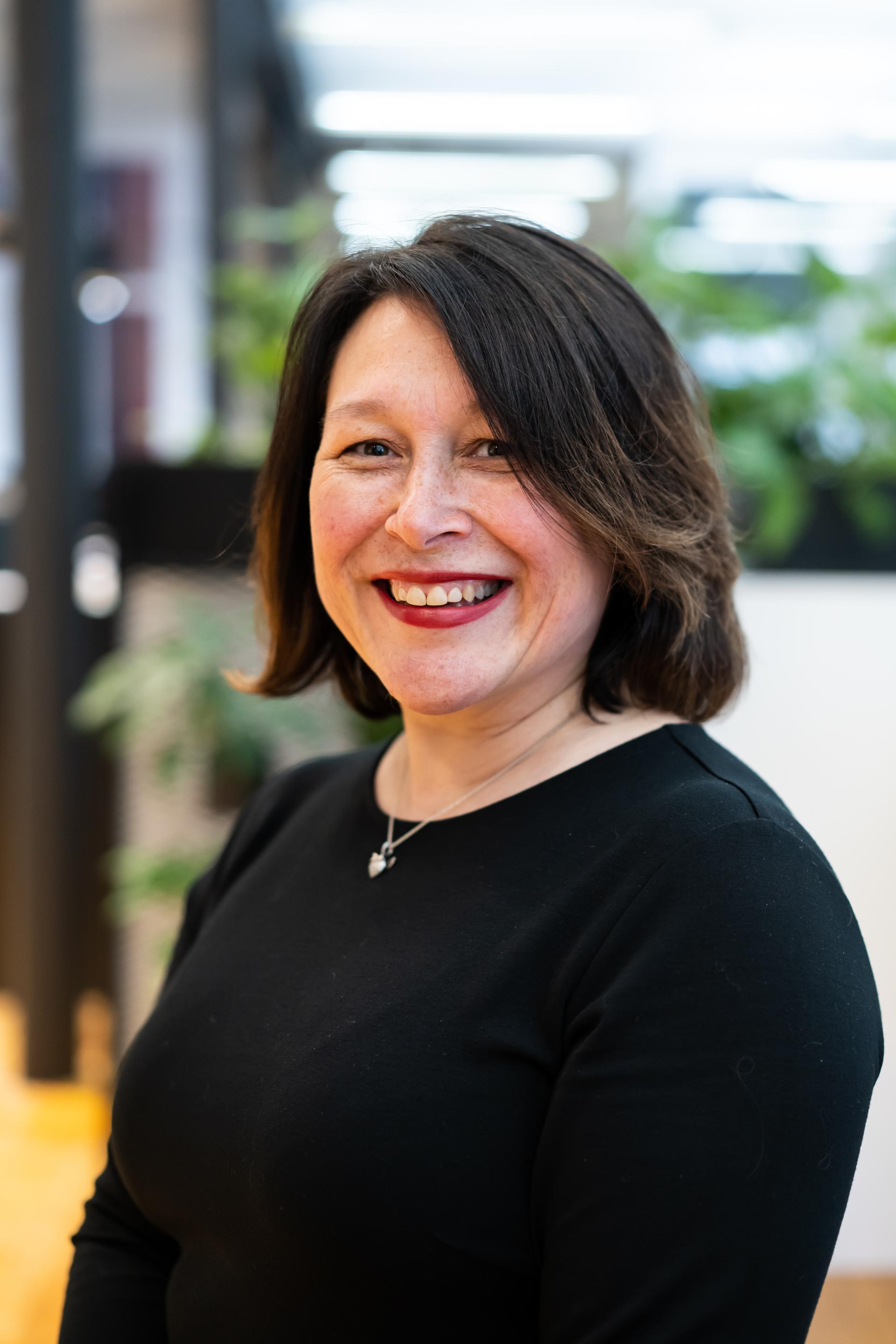 Portrait of a smiling woman in a black top, representing professionals in the sustainable built environment sector.