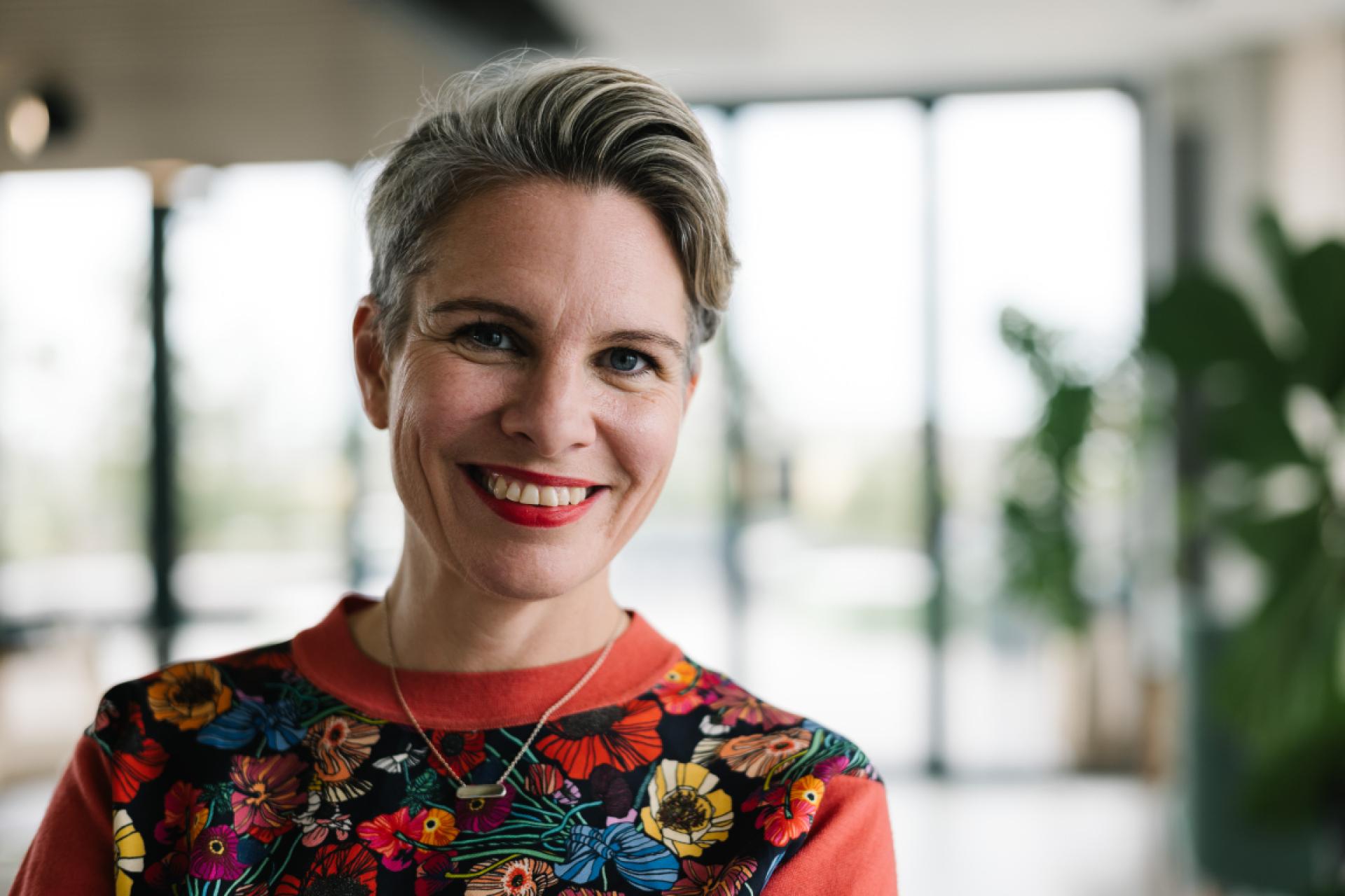 Smiling woman wearing a colorful floral sweater, reflecting on diverse interviews throughout the year in a modern interior setting.
