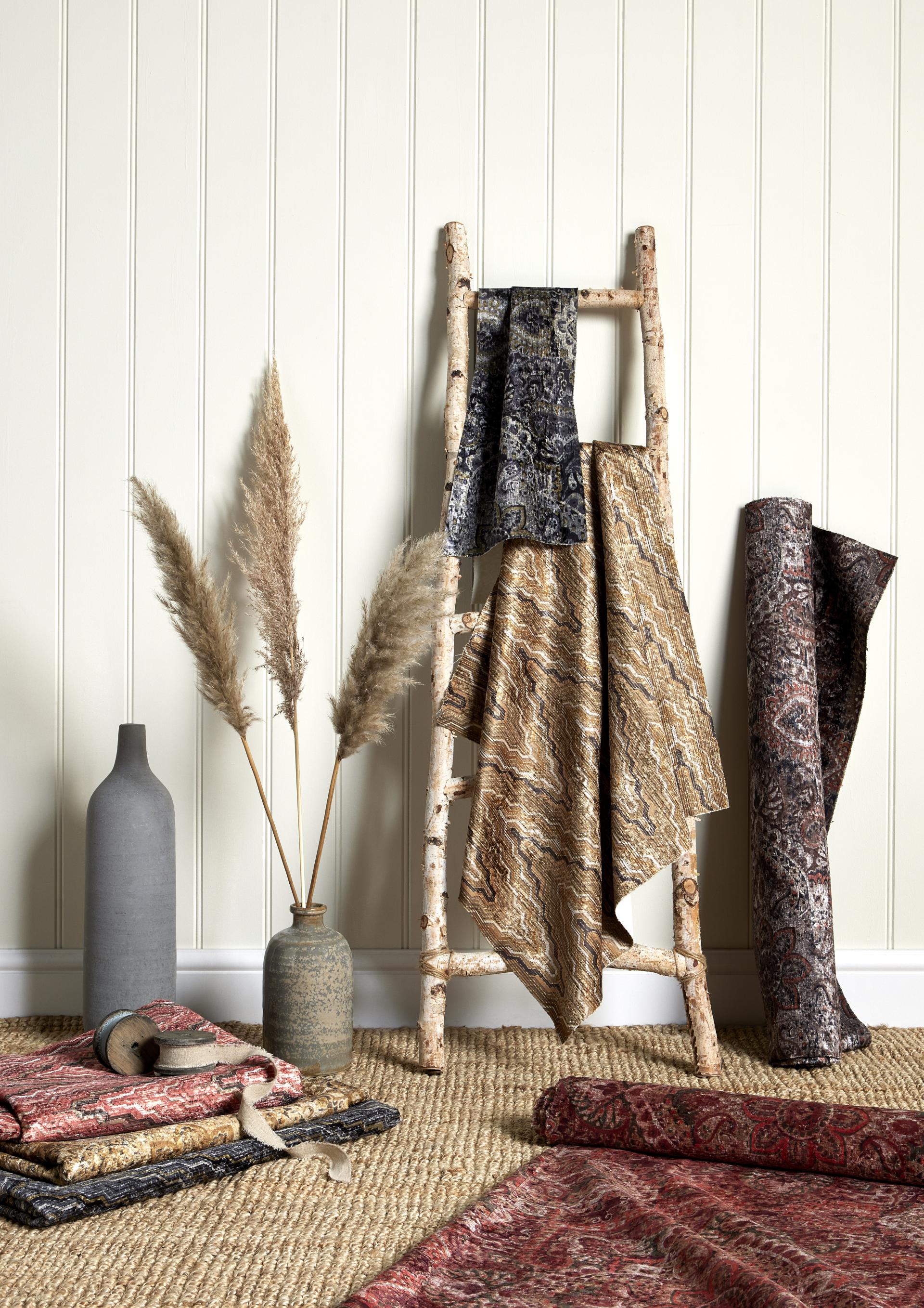 Luxurious structured jacquard fabrics from Panaz displayed on a wooden ladder alongside decorative vases and natural elements.