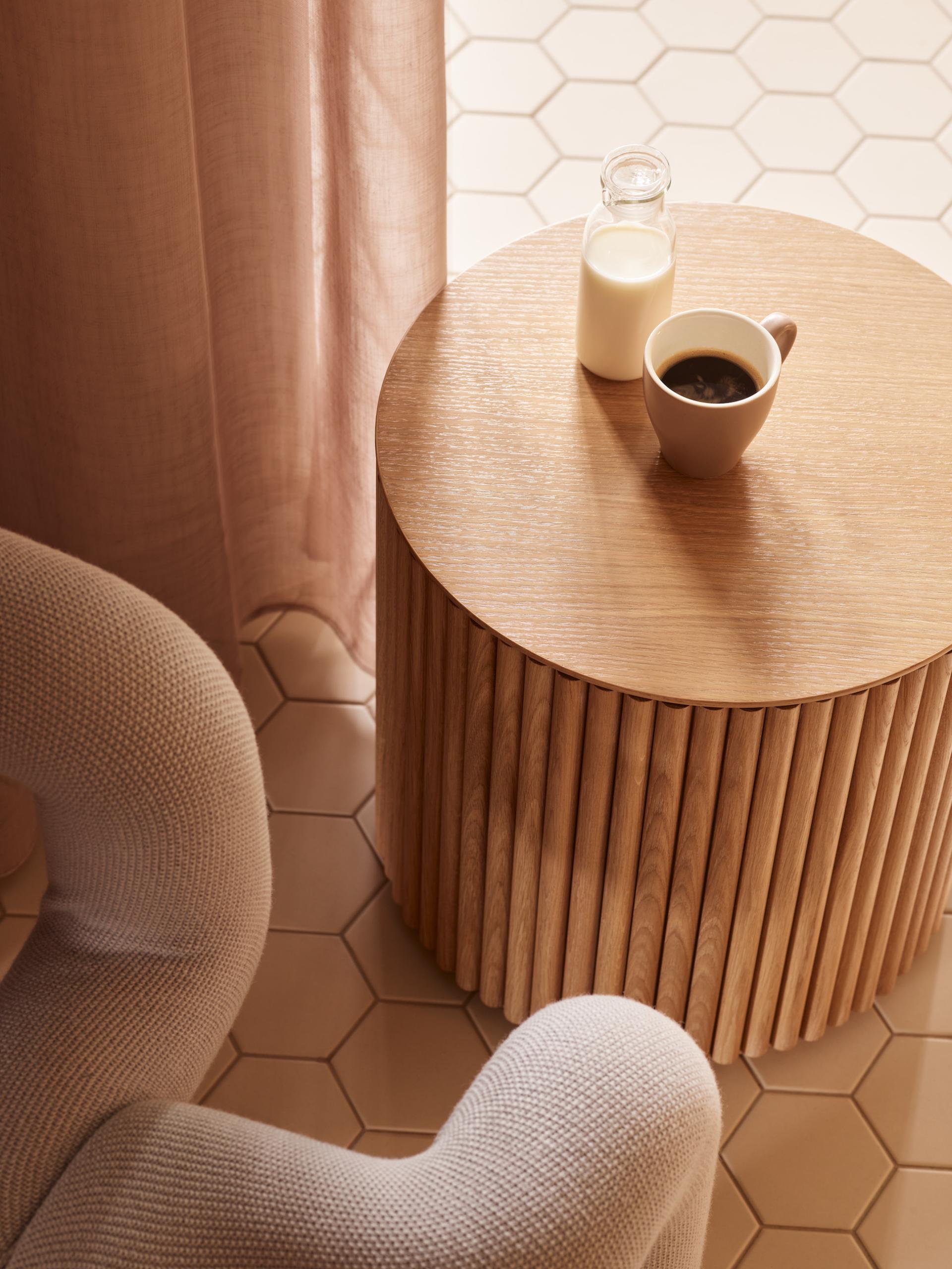 Stylish workspace with a wooden side table, coffee cup, and milk bottle, reflecting Liberty House's modern design.