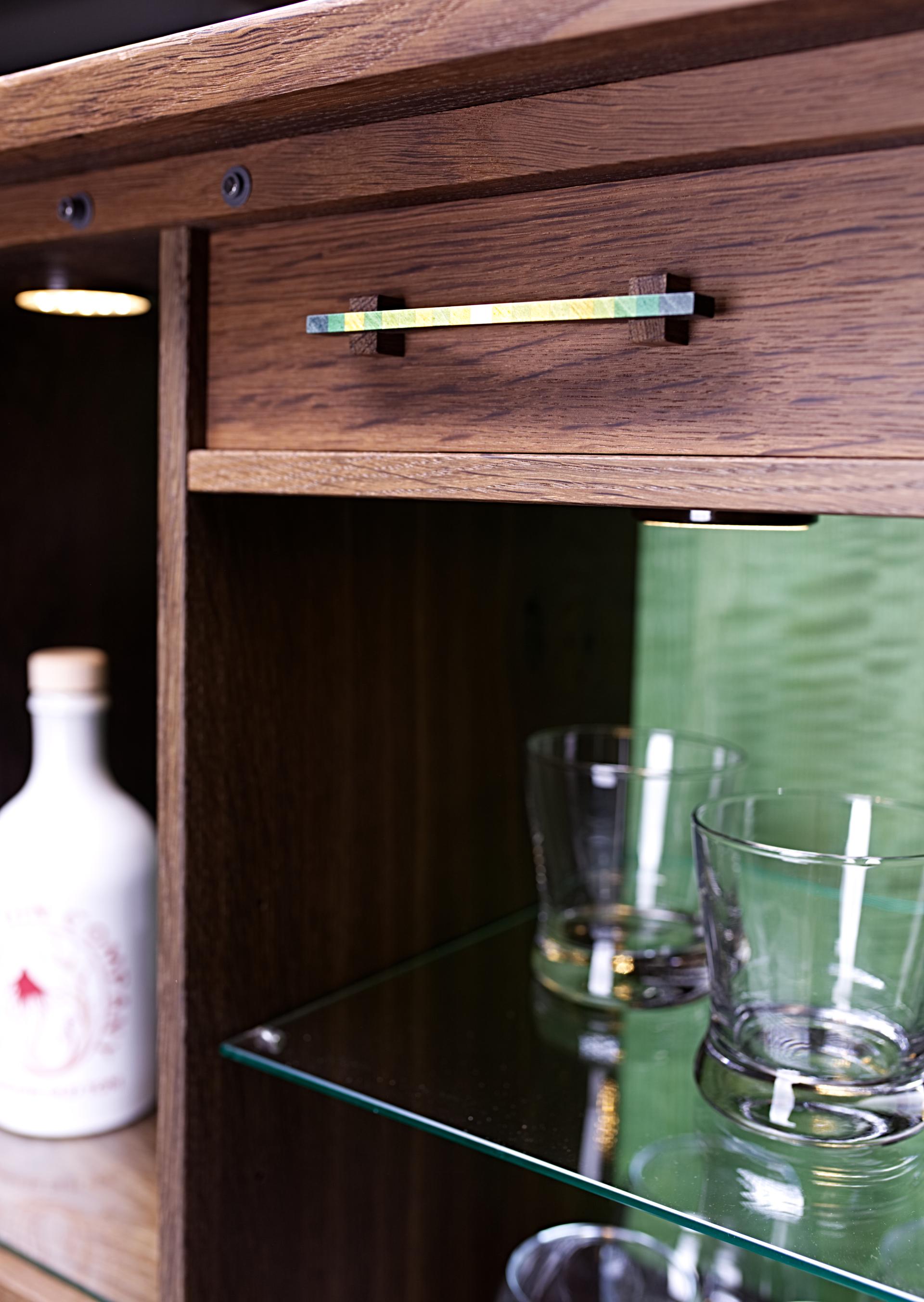 Stylish wooden cabinet with colorful handle, glass shelves, and decorative glassware, inspired by Madeira's natural beauty.