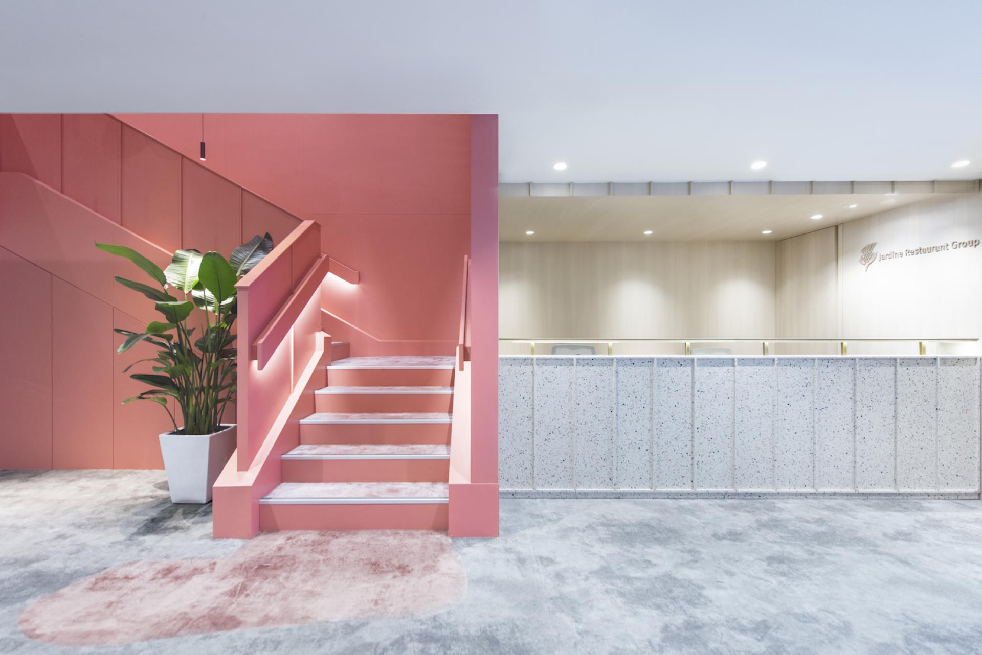Modern workspace design featuring a pink stairway, greenery, and a reception area for Jardine Restaurant Group by Bean Buro.