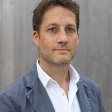Nic Crawley, architect and designer, poses confidently in a tailored jacket, discussing cross-laminated timber architecture.