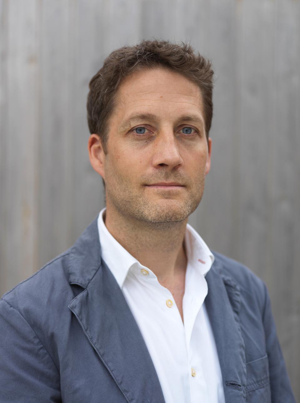 Nic Crawley, architect and designer, poses confidently in a tailored jacket, discussing cross-laminated timber architecture.