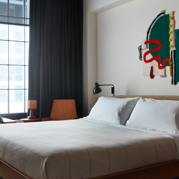 Stylish Ace Hotel Brooklyn guest room featuring contemporary decor, large windows, and an artistic wall hanging.