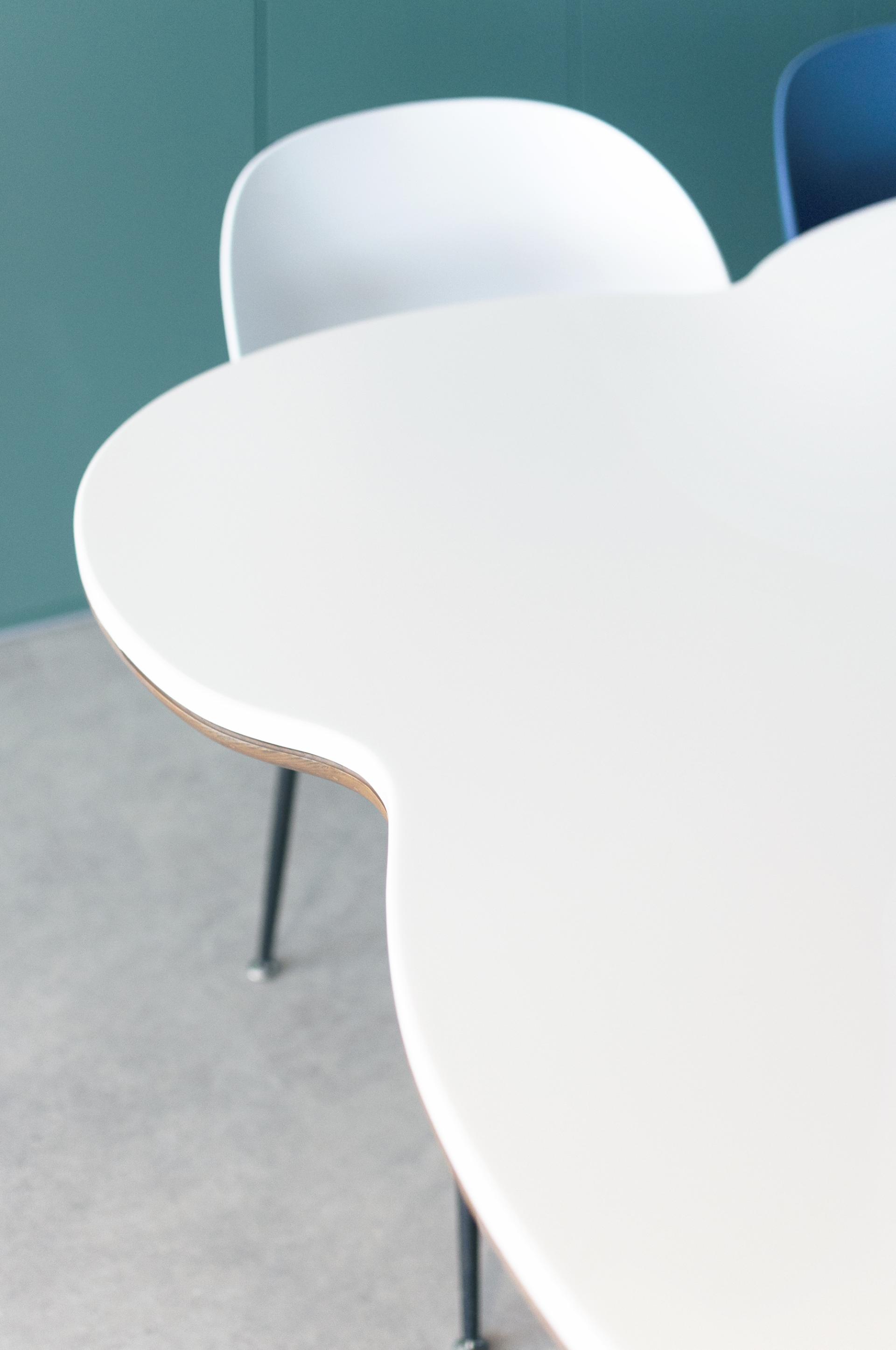 Child-friendly, organic-shaped white table with colorful chairs in a modern paediatric clinic designed for wellbeing.