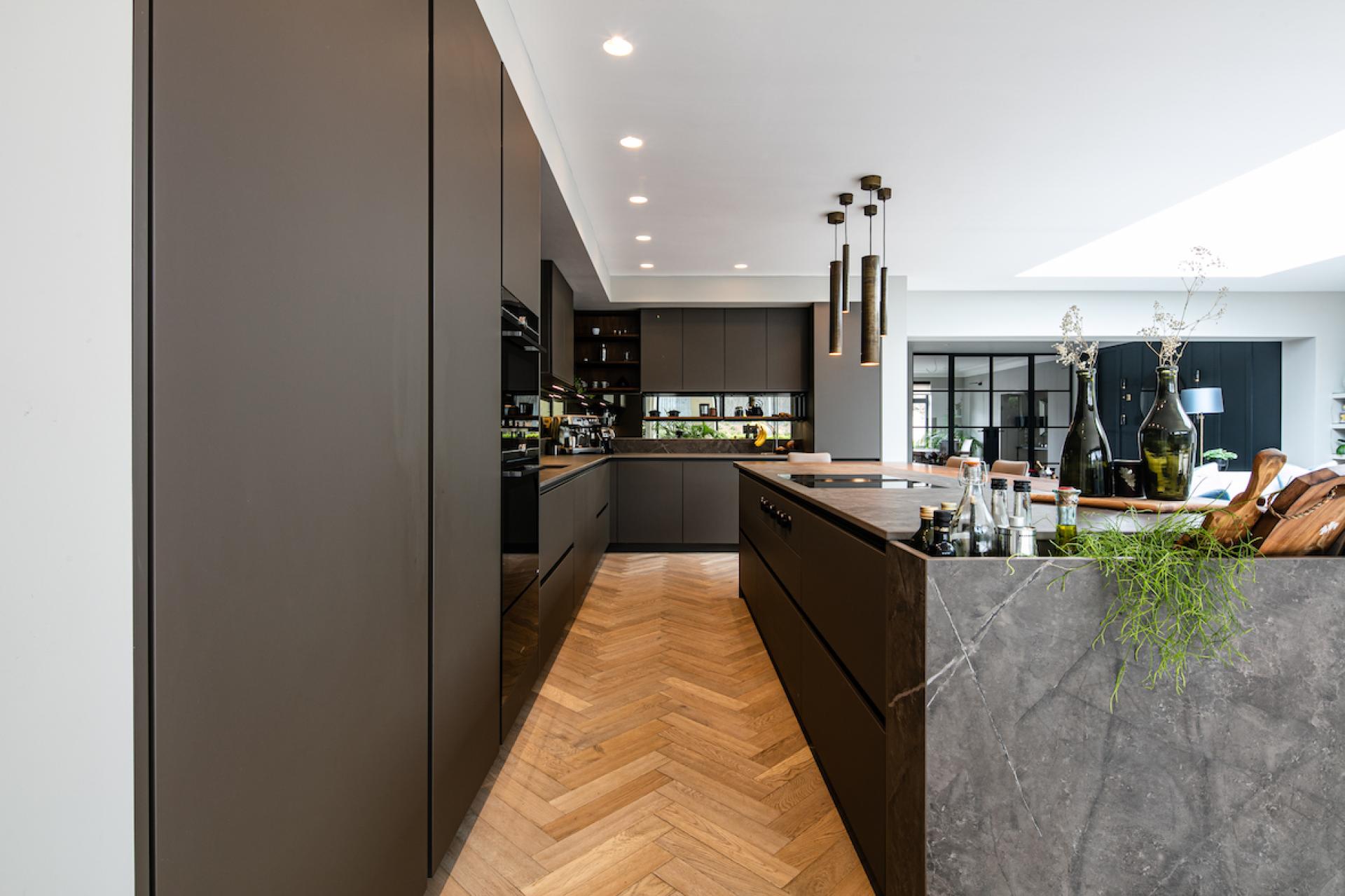 Modern kitchen featuring a multifunctional design with contrasting Dekton surfaces, sleek cabinetry, and warm wood flooring.