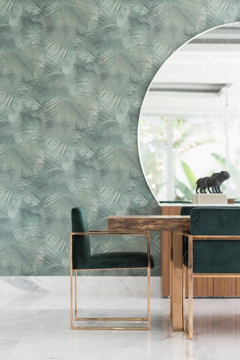 Elegant dining area featuring minimalistic design, green velvet chairs, and a textured botanical wallpaper backdrop.