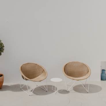 Stylish Acapulco chairs and a minimalist table create a serene outdoor space, harmonizing with nature and contemporary design.