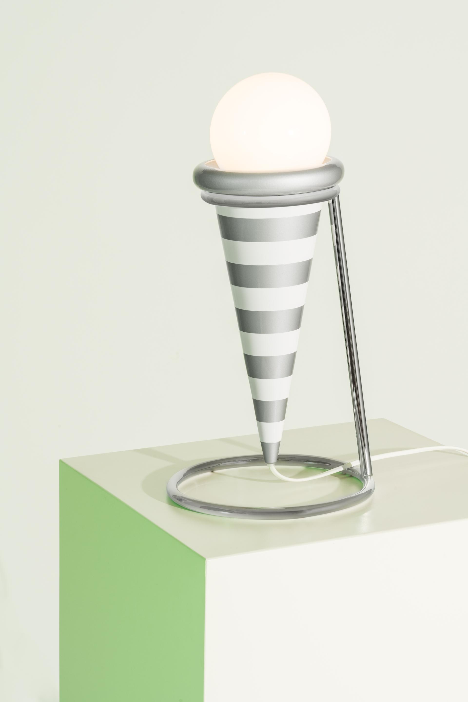 A modern striped cone lamp with a spherical light sits on a colorful pedestal, showcasing Memphis movement design.