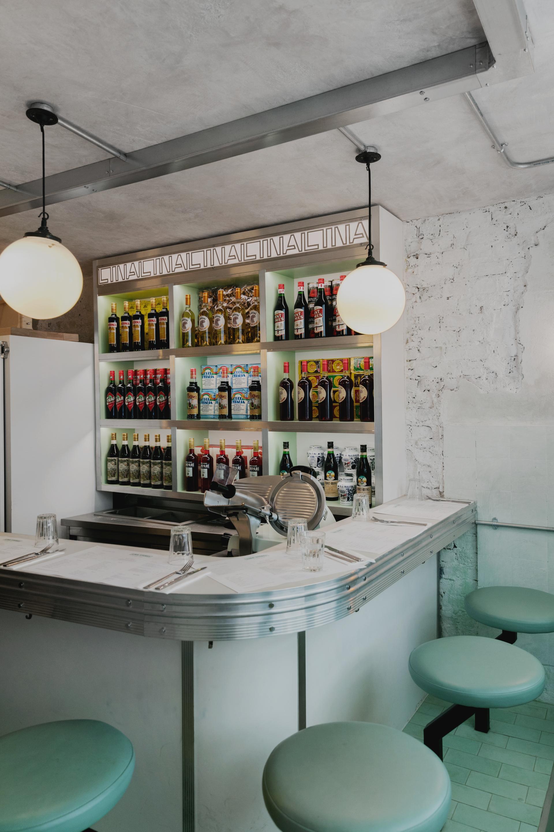 Art Deco-inspired Italian restaurant bar featuring green and white striped decor, shelves of beverages, and sleek seating.