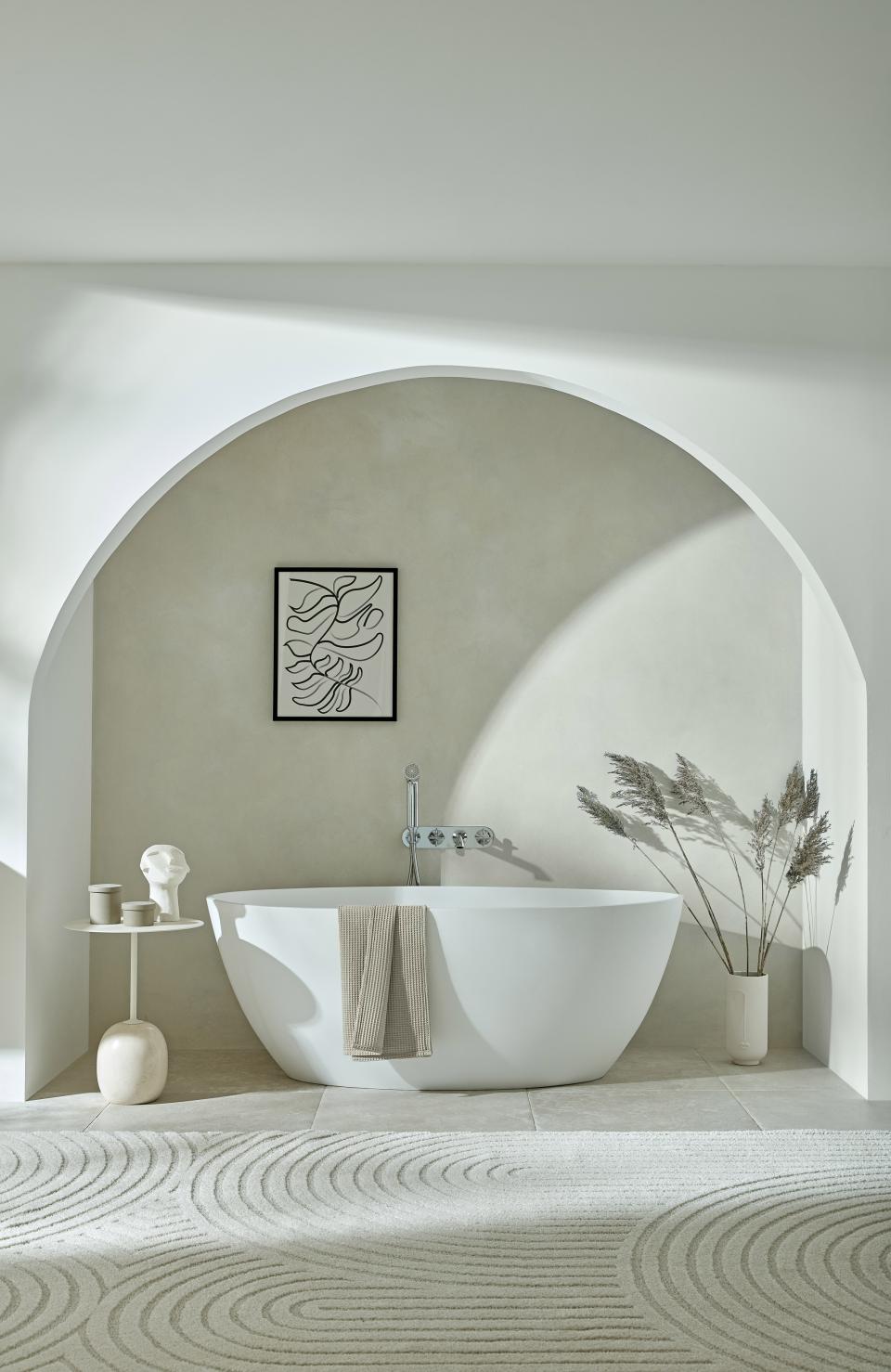 Elegant bathroom featuring a sleek white bathtub, minimalist decor, and an artistic wall hanging in natural light.