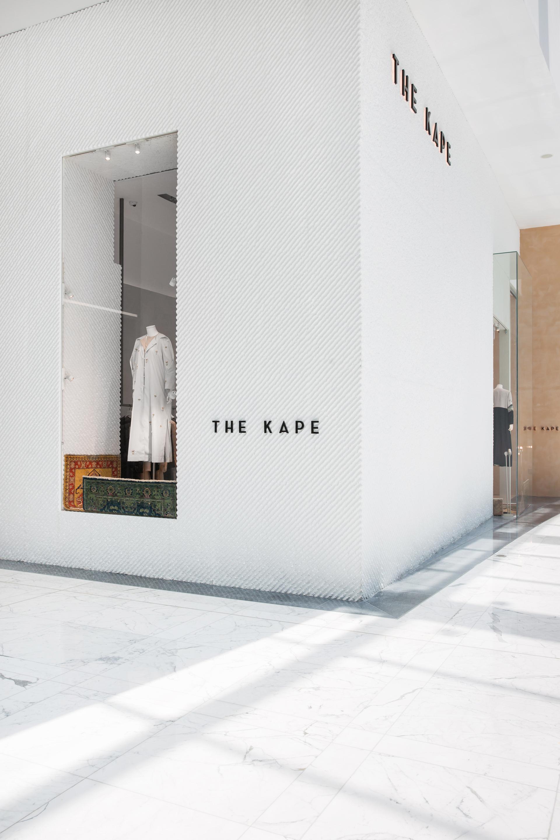Modern retail display of THE KAPE featuring modest women's fashion, with a chic white wall and elegant lighting.