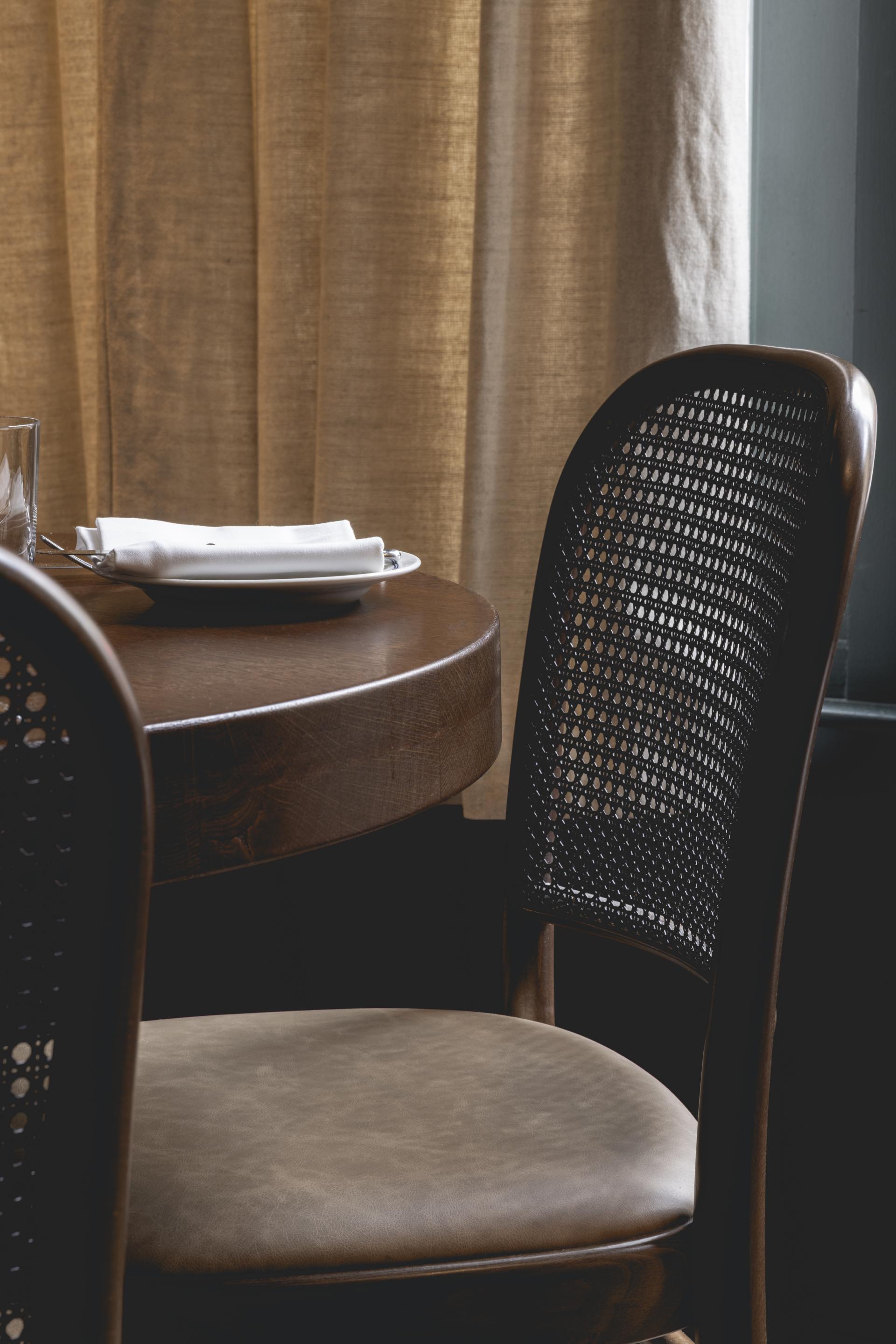 Elegant wooden chair next to a round table set with white napkins, echoing Parisian chic in a rustic setting.