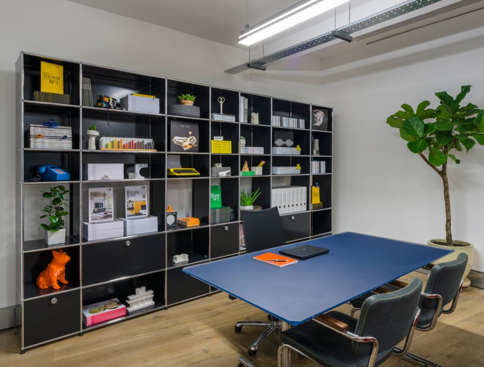 Modern Clerkenwell showroom featuring modular furniture, a stylish black shelving unit, and a blue conference table with seating.