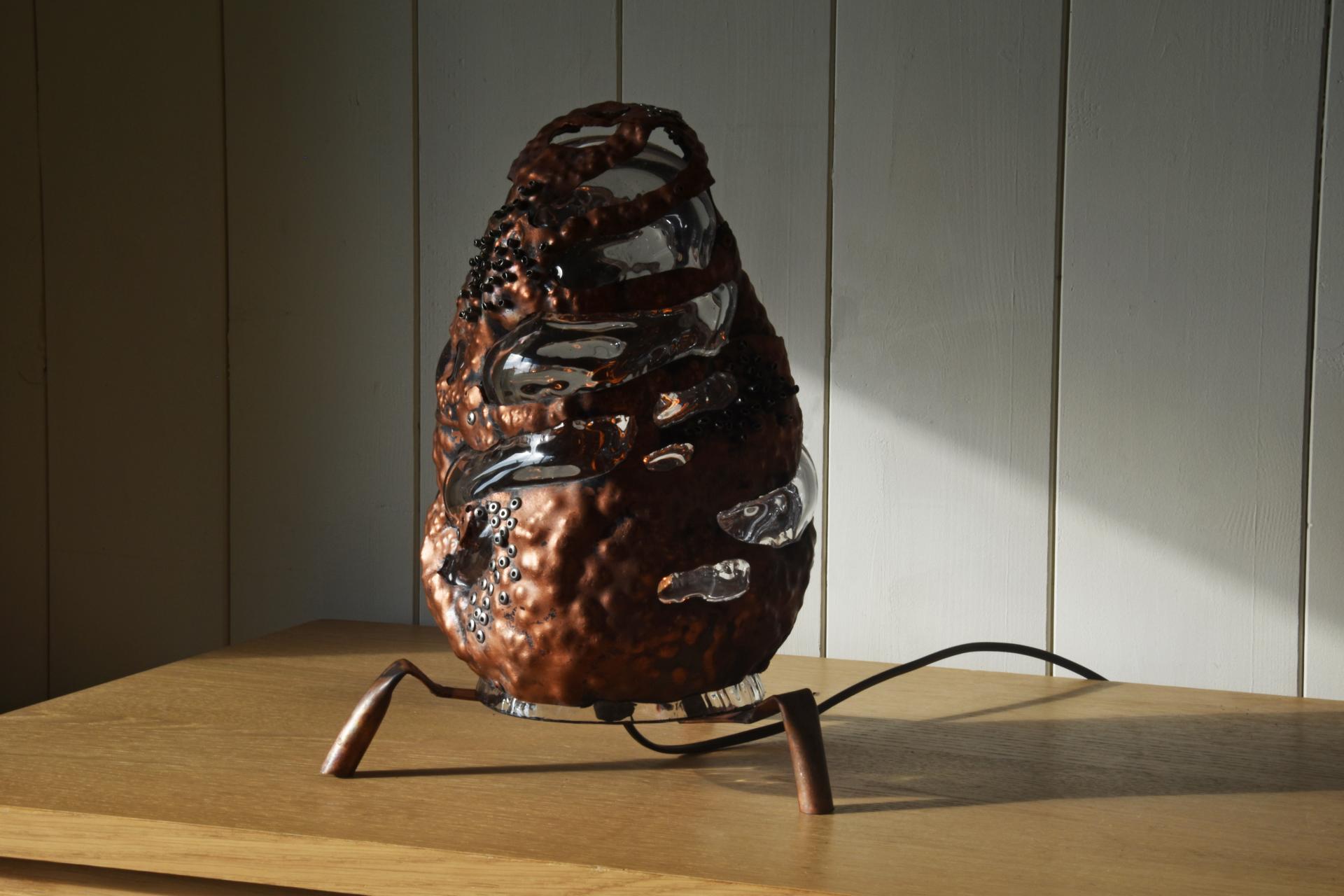 Unique contemporary lamp design featuring a textured copper finish and glass elements, showcased at Milestones exhibition.