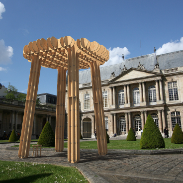 Wooden architectural installation in a Paris courtyard, showcasing innovative design amidst historic buildings and landscaped greenery.