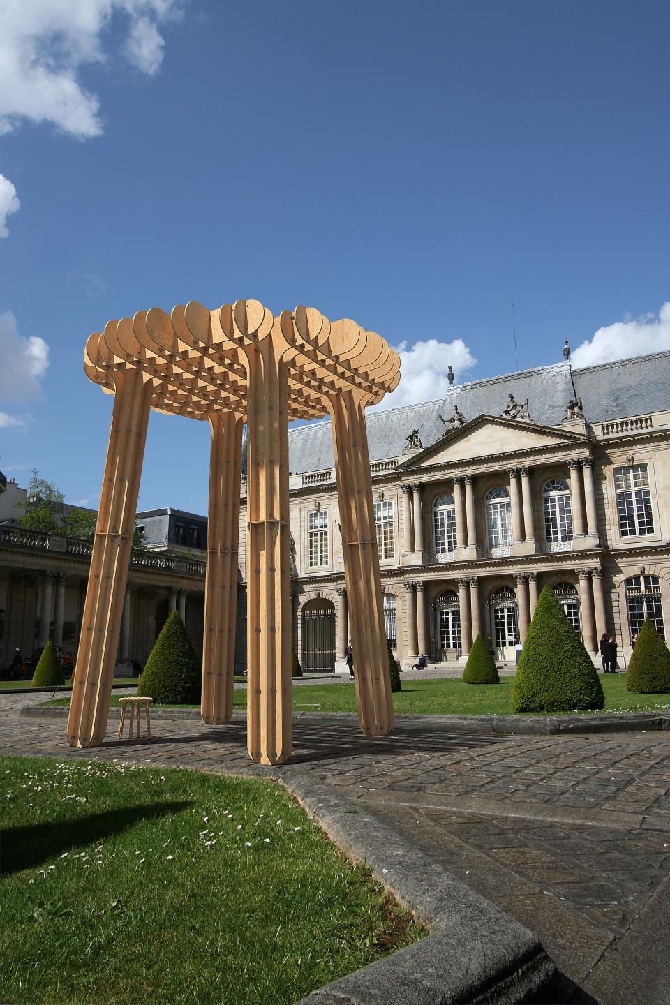 Wooden architectural installation in a Paris courtyard, showcasing innovative design amidst historic buildings and landscaped greenery.
